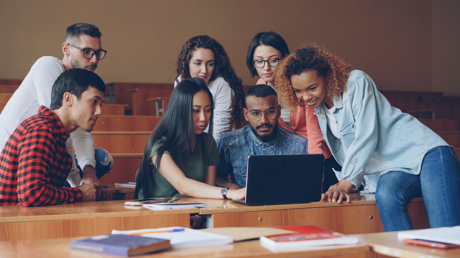 A diverse group of college students gathered around a laptop