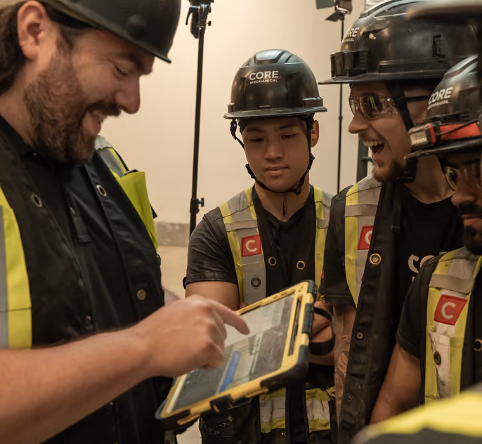 Group of construction workers in safety gear reviewing information on a rugged tablet.