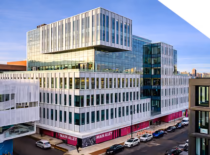 Modern multi-story glass and white office building on a city street with parked cars.