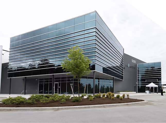 Modern office building with reflective glass walls and landscaped greenery in front.