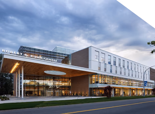 Robert G. Kuhn Centre building with large glass facade and modern design under a cloudy sky at dusk.