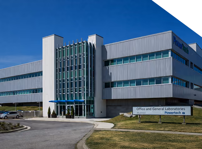 Modern gray office building with glass entrance and sign reading Office and General Laboratories Powertech.