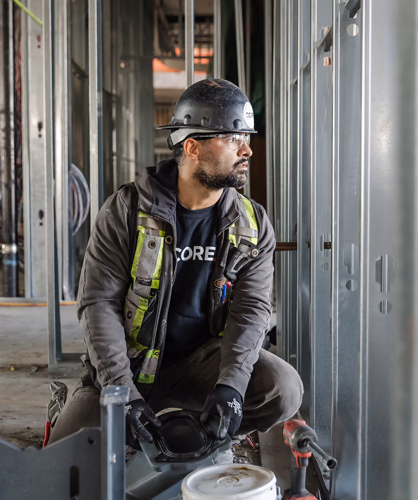 Construction worker wearing a hard hat and gloves kneeling inside a building under construction.