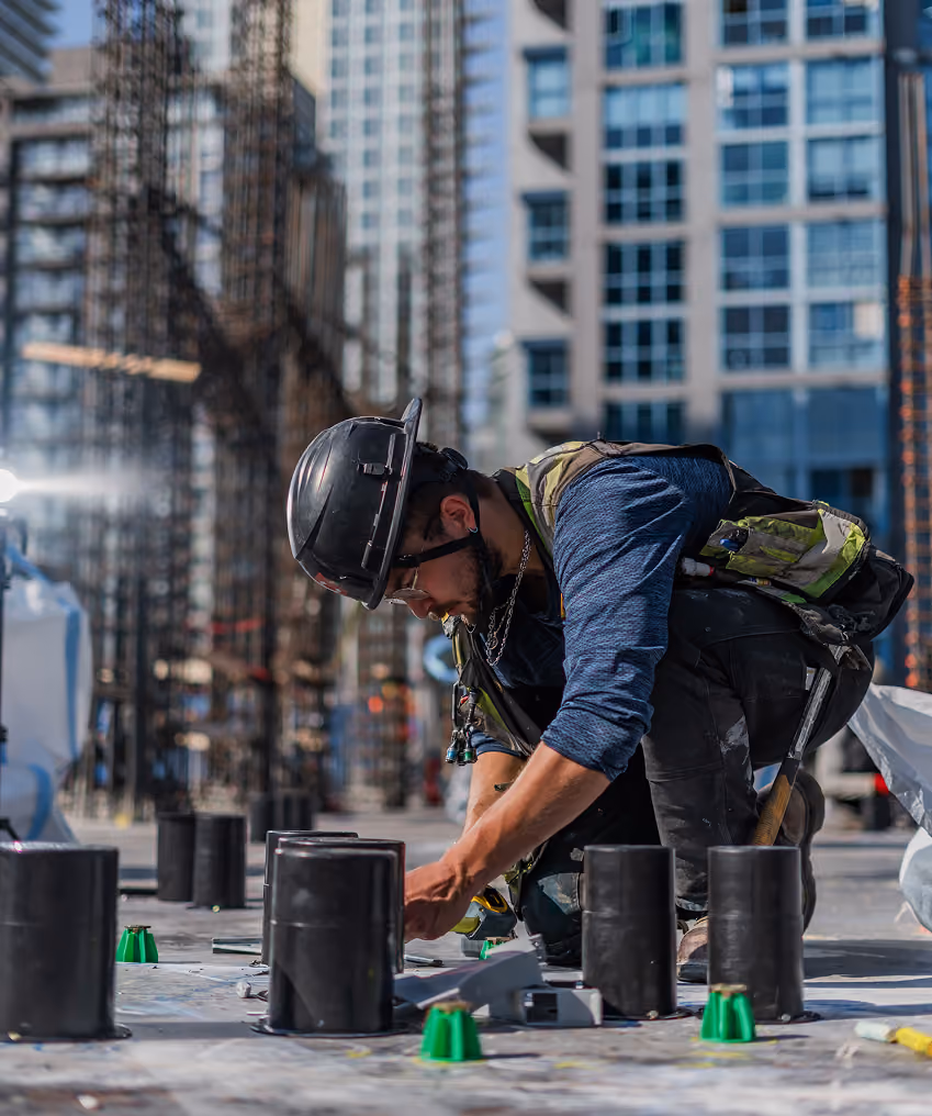 Construction worker in hard hat kneeling and working on pipes at urban building site.