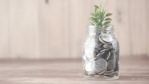 Alcancía de vidrio con monedas y una planta creciendo, simbolizando el crecimiento del ahorro con Betterplan