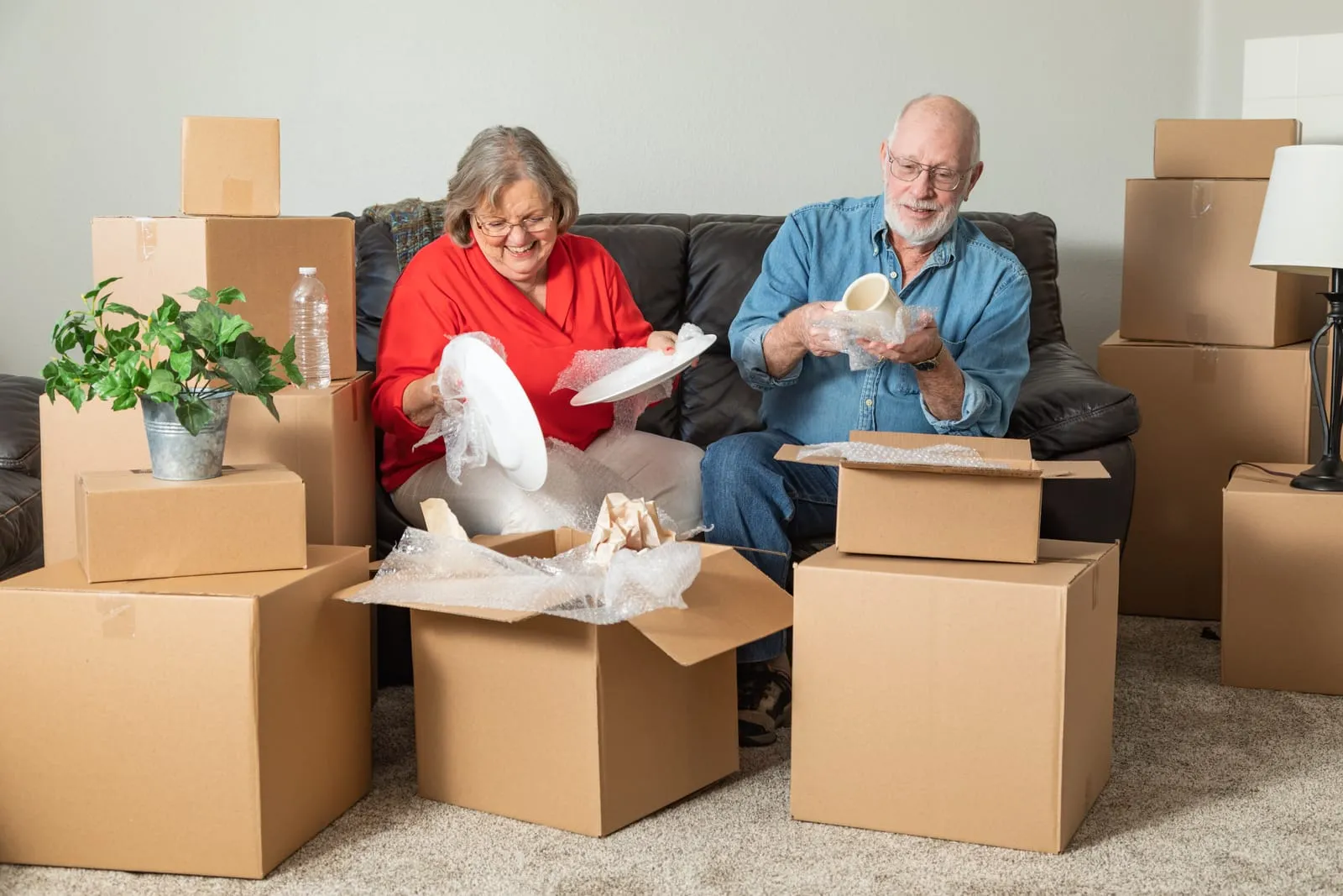 Senior couple carefully wrapping dishes in bubble wrap, discussing packing services for seniors