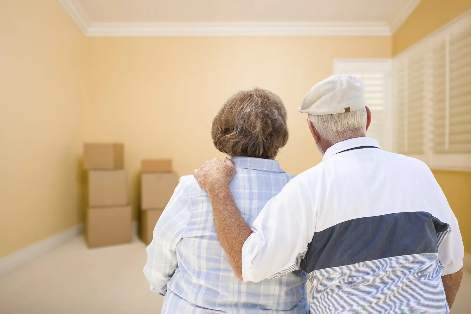Elderly couple standing together looking at packed boxes in their room after using packing services for seniors