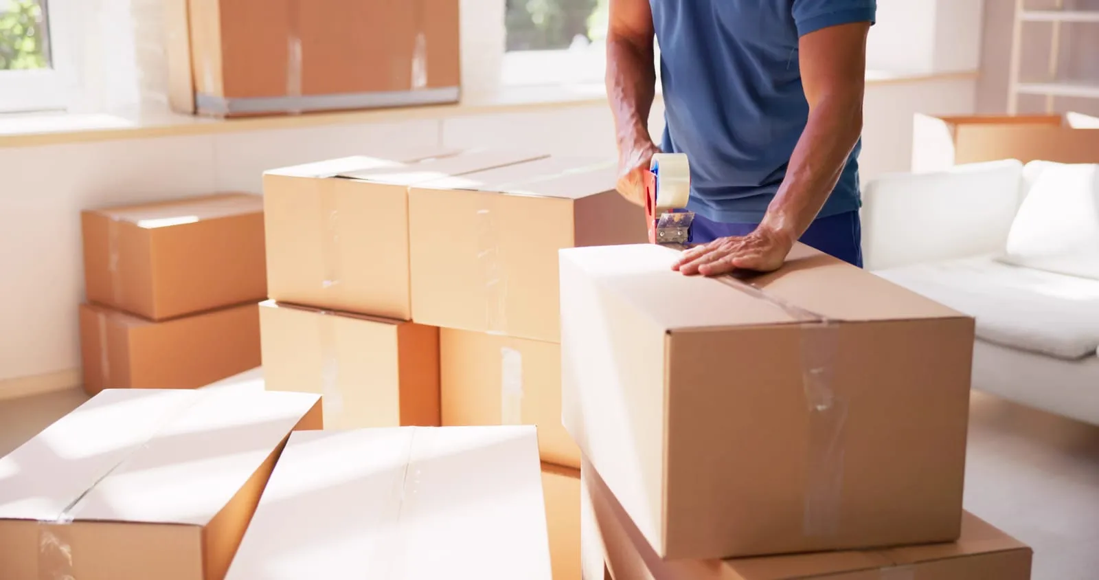 Professional mover using a tape dispenser to seal moving boxes as part of packing services for seniors.