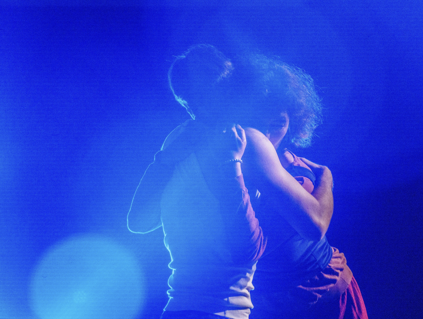 Deux personnes s'enlaçant sous une lumière bleue intense dans une atmosphère obscure.