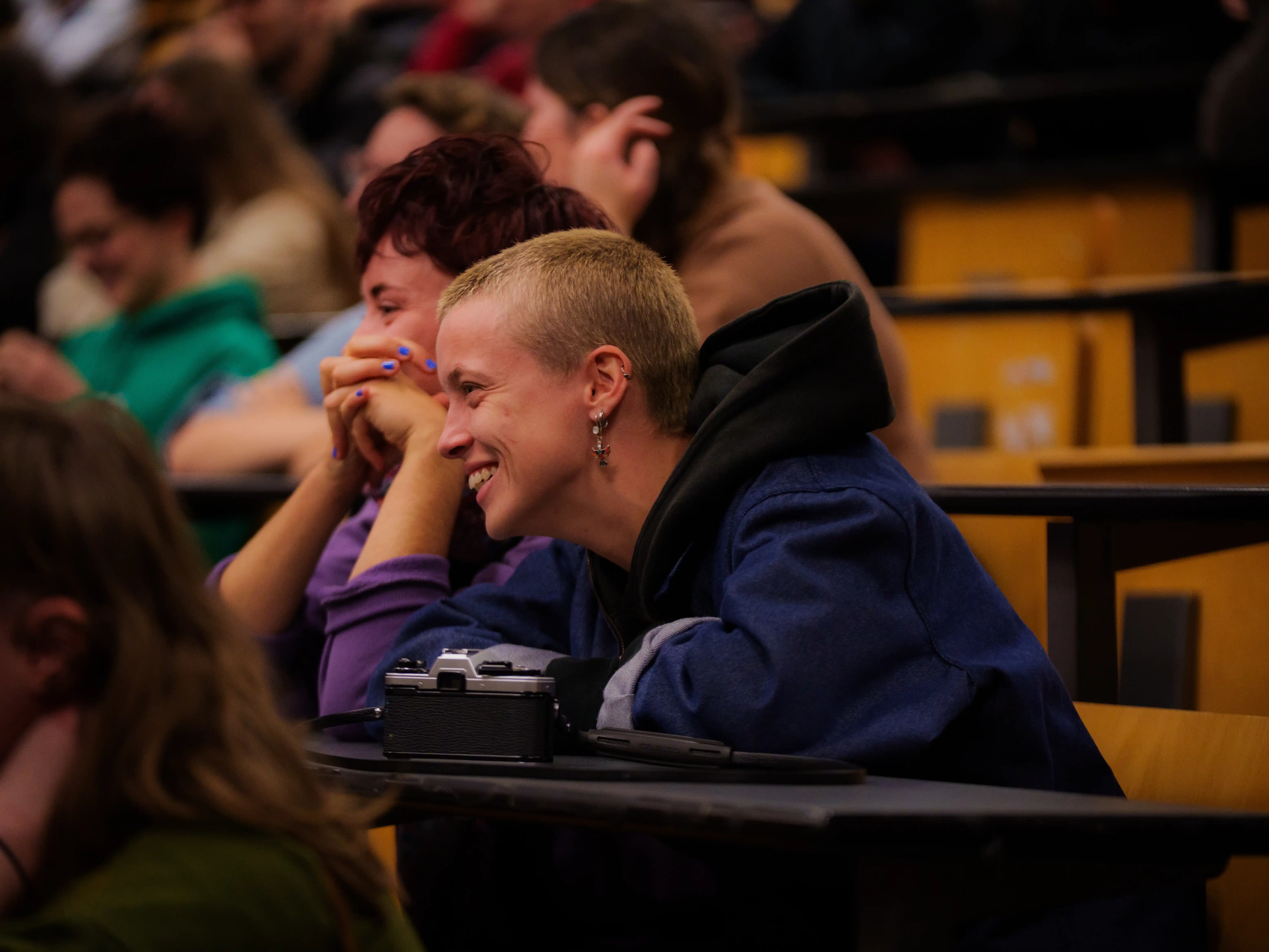 Jeunes assis dans une salle de classe, souriant et discutant, avec un appareil photo argentique sur le bureau.