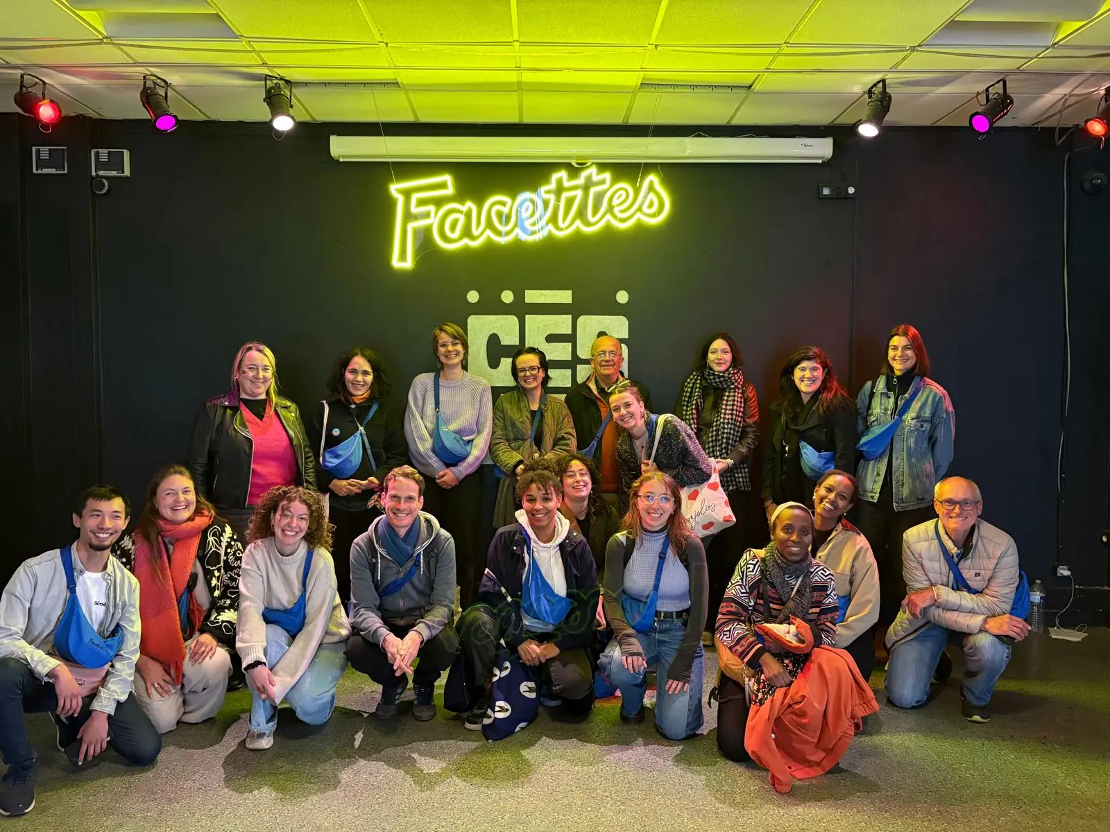 Groupe de personnes posant devant un mur noir avec un néon jaune affichant le mot "Facettes".