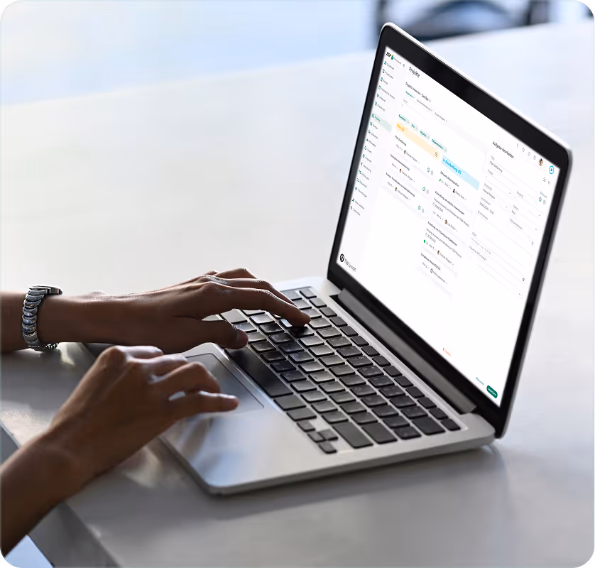 Person tippt auf einem Laptop mit Finanz- oder Budgetplanungs-Software neben einem Smartphone und Notizbuch auf einem Tisch.