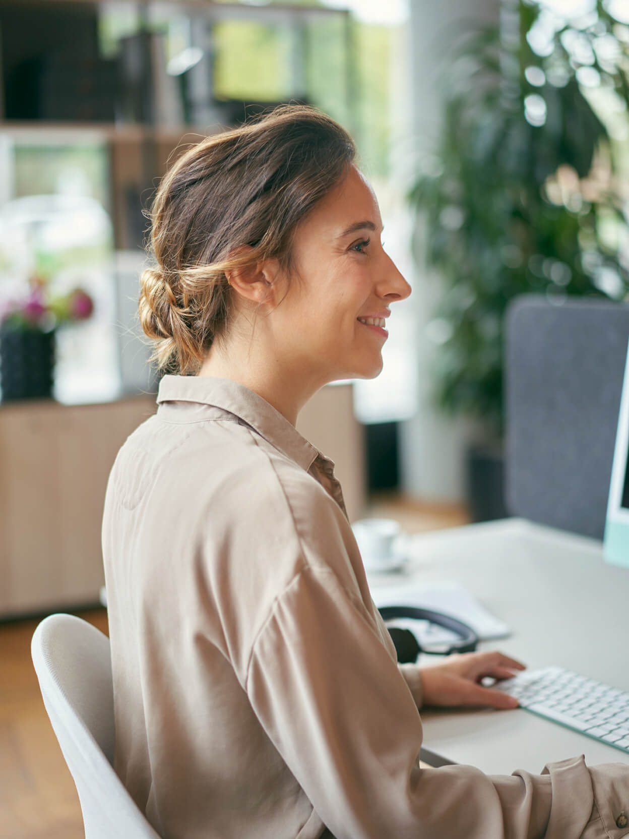 Frau sitzt lächelnd am Schreibtisch und arbeitet am Computer