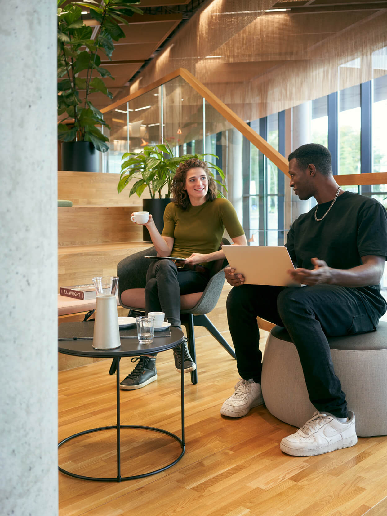 Zwei Personen im Gespräch in moderner Loungezone mit Laptop und Kaffee
