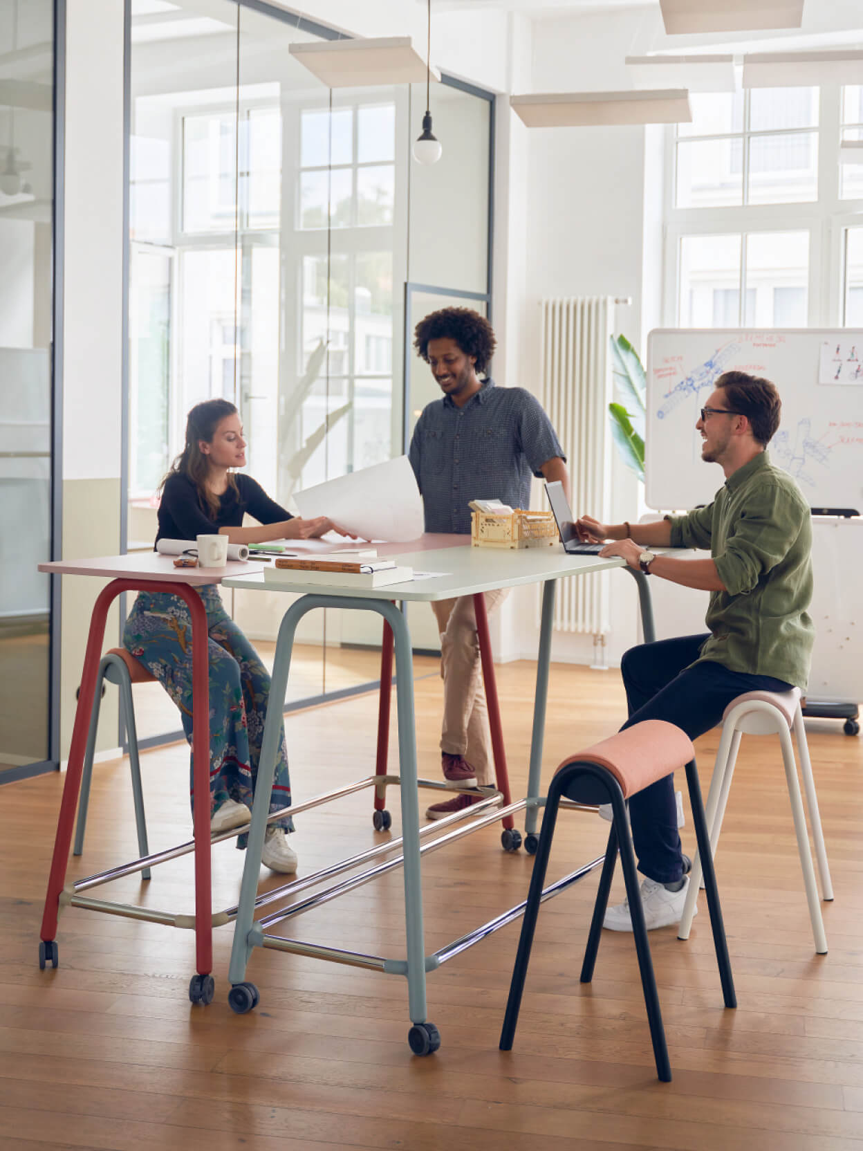 Drei Personen arbeiten gemeinsam an einem Stehtisch in hellem Büro