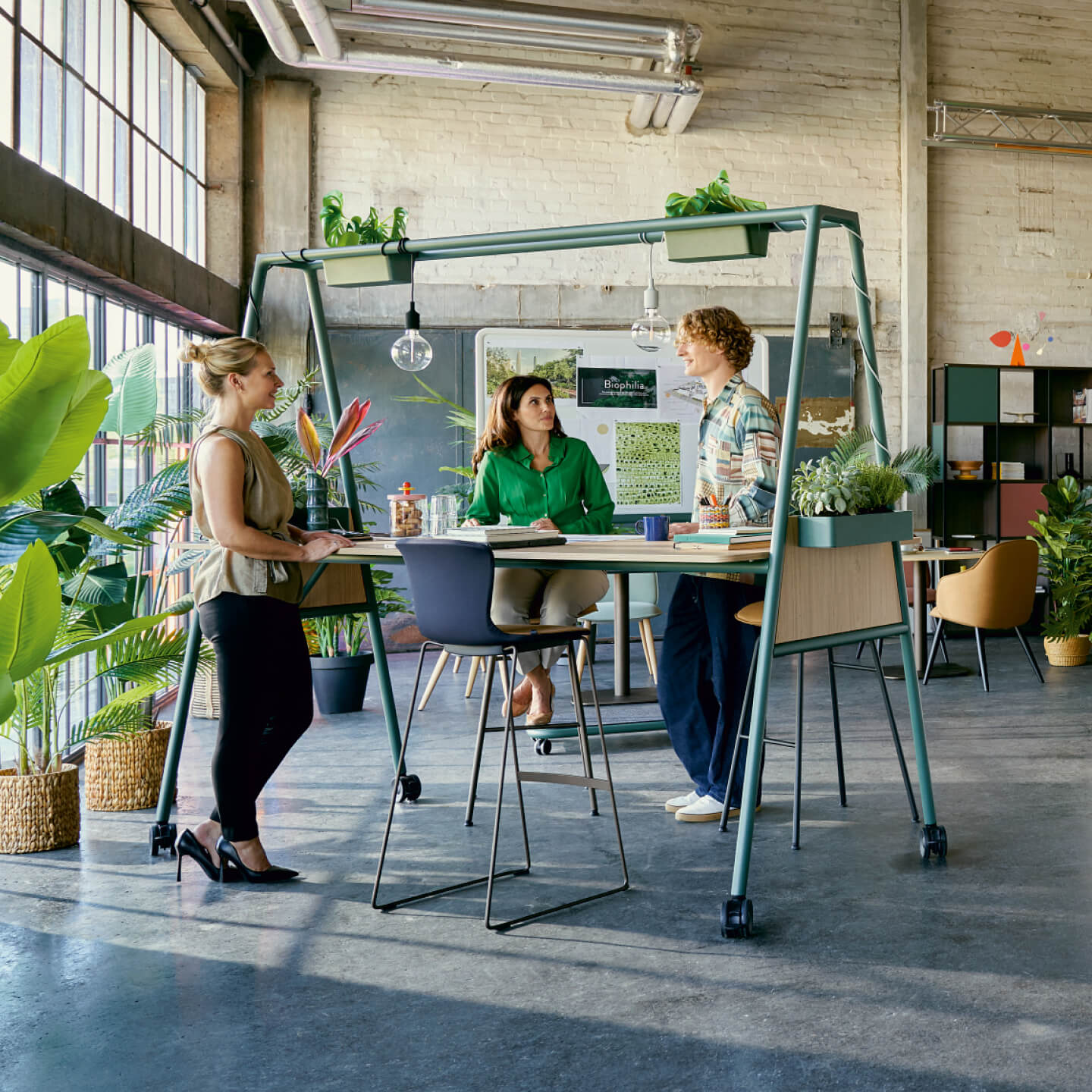 Drei Personen im Austausch an einem begrünten Stehtisch in modernem Büro