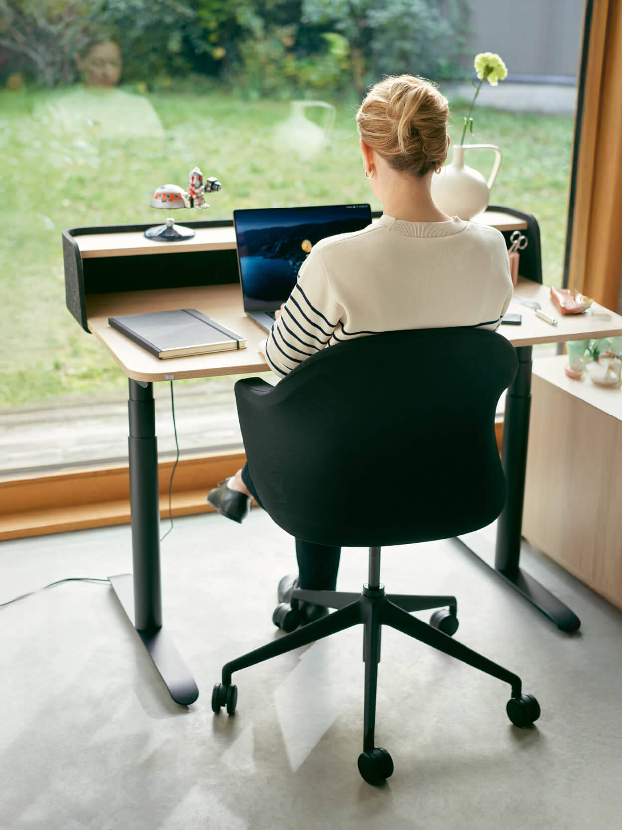 Frau arbeitet am Laptop an einem höhenverstellbaren Schreibtisch mit Blick ins Grüne