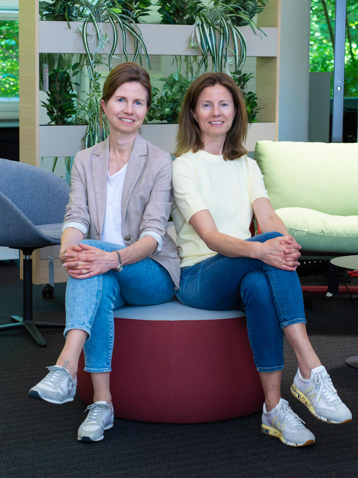 Die zwei Geschäftsführerinnen sitzen entspannt in moderner Büro-Lounge