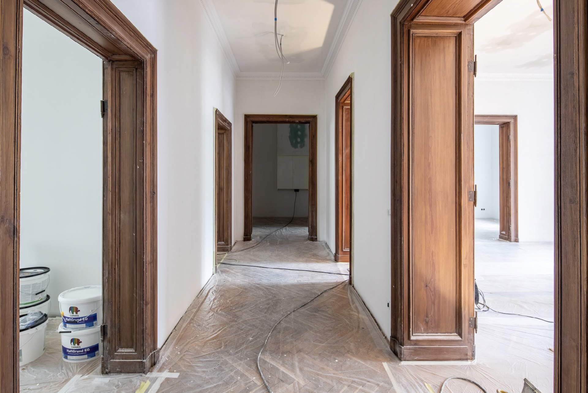 Flur mit weiß gestrichenen Wänden und Holztürrahmen während einer Renovierung.