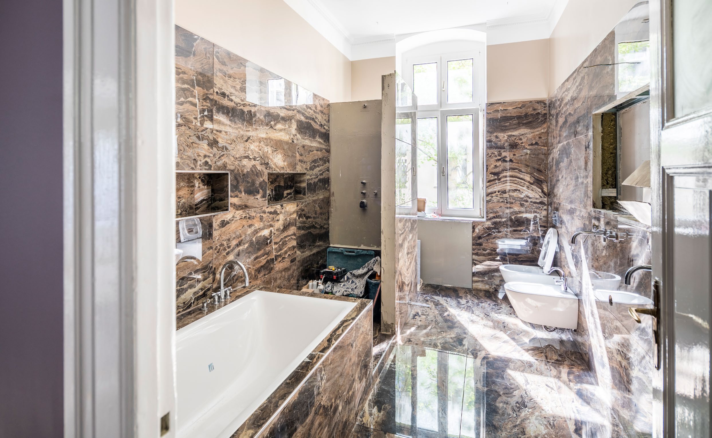 Luxuriöses Badezimmer mit braunem Marmorboden, Badewanne, WC, Bidet und großem Fenster.