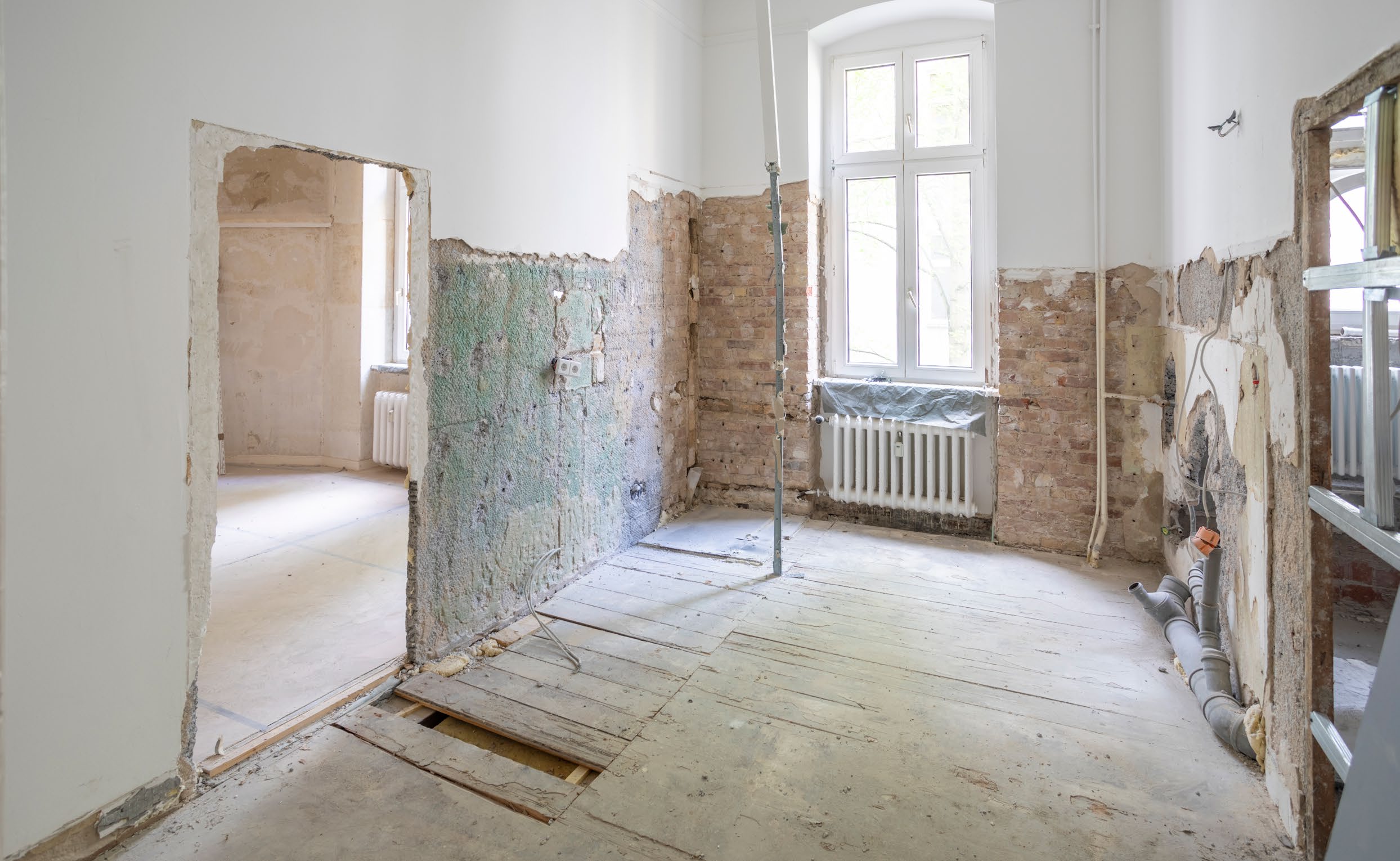 Renovierungsbedürftiger Altbau-Raum mit freigelegten Wänden, alter Heizung und offenem Boden.