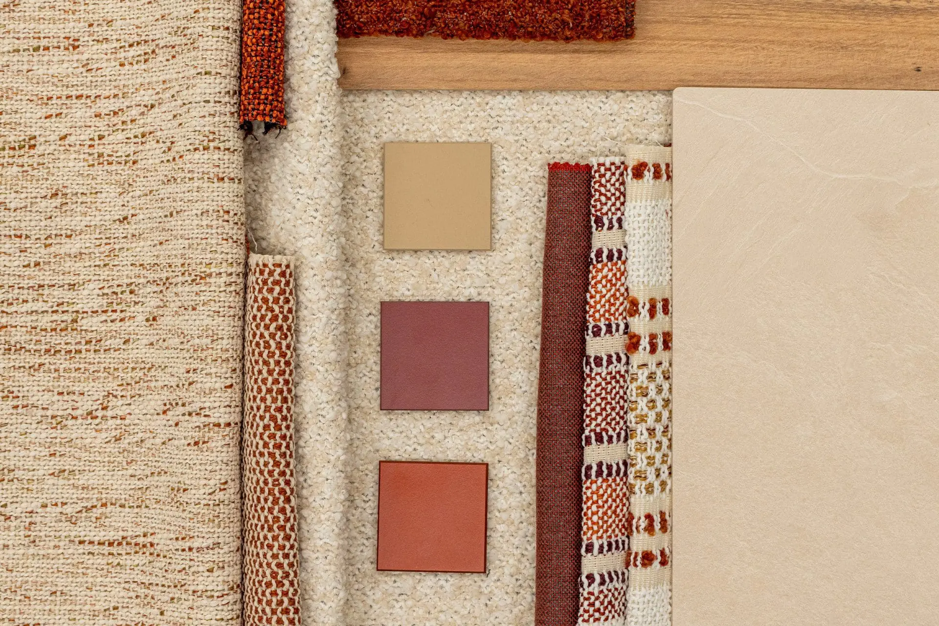 Verschiedene beige, braune und rote Stoffproben und Materialmuster auf hellem Hintergrund, darunter Holz-, Textil- und Fliesenmuster.