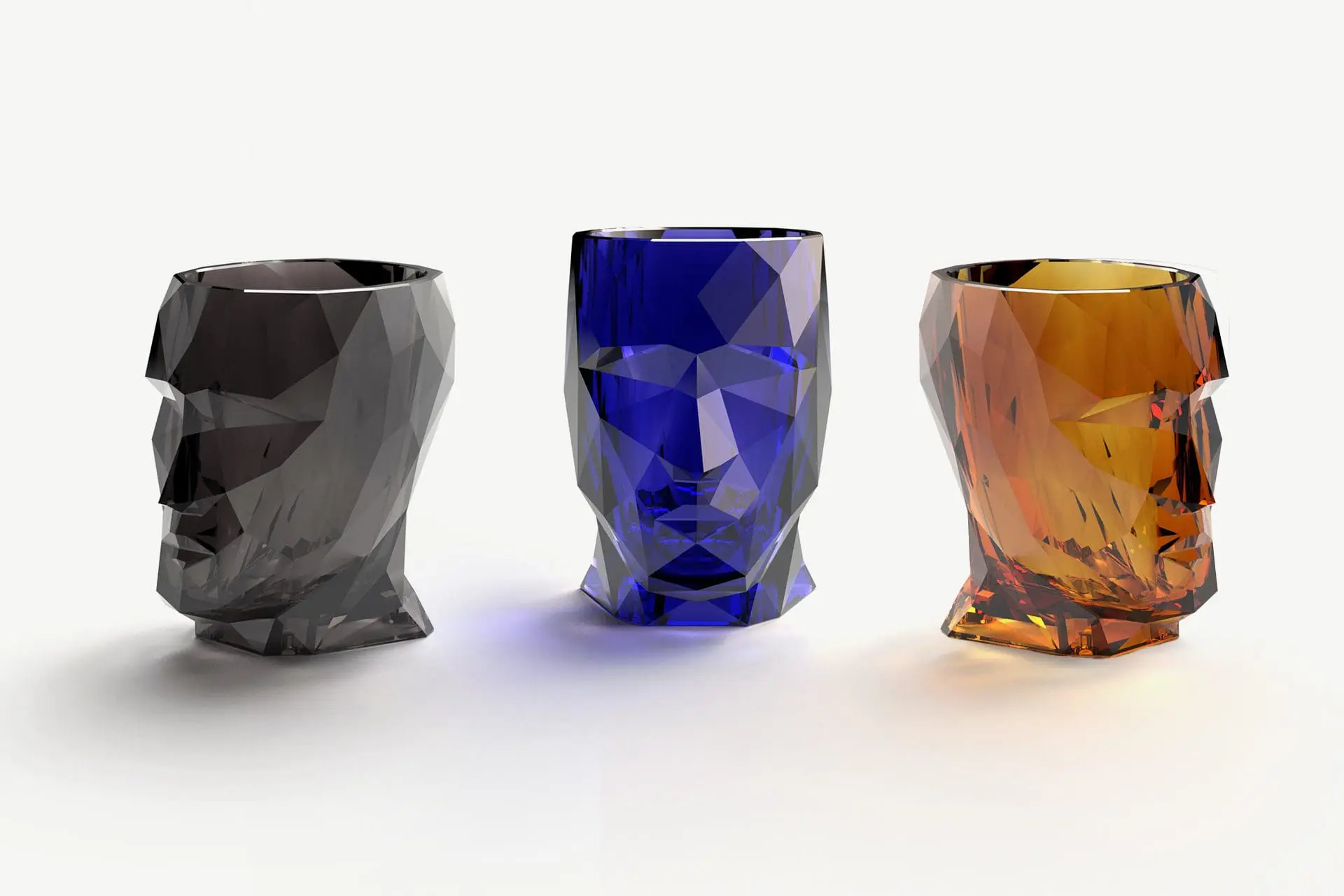 Drei geometrisch facettierte, gläserne Trinkgefäße in Form von Köpfen in Schwarz, Blau und Bernsteinfarben.