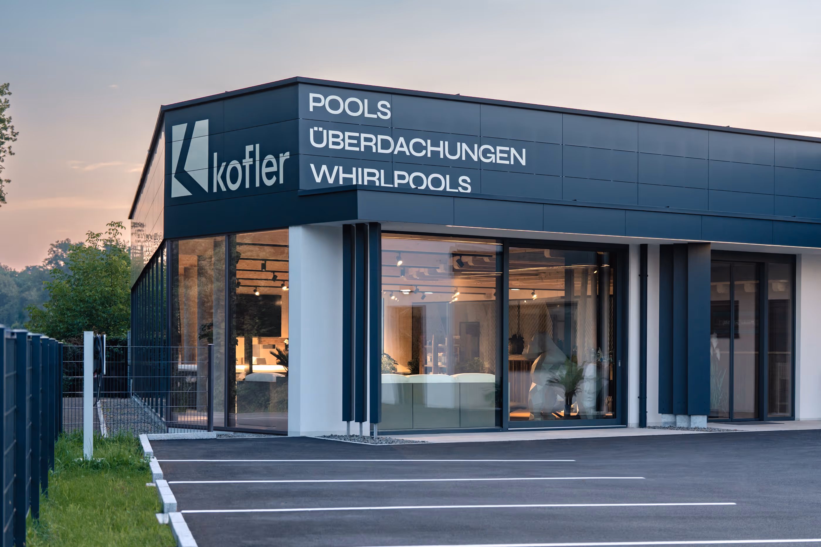Modernes Gebäude mit Glasfront und Kofler-Logo, das Pools, Überdachungen und Whirlpools anbietet.