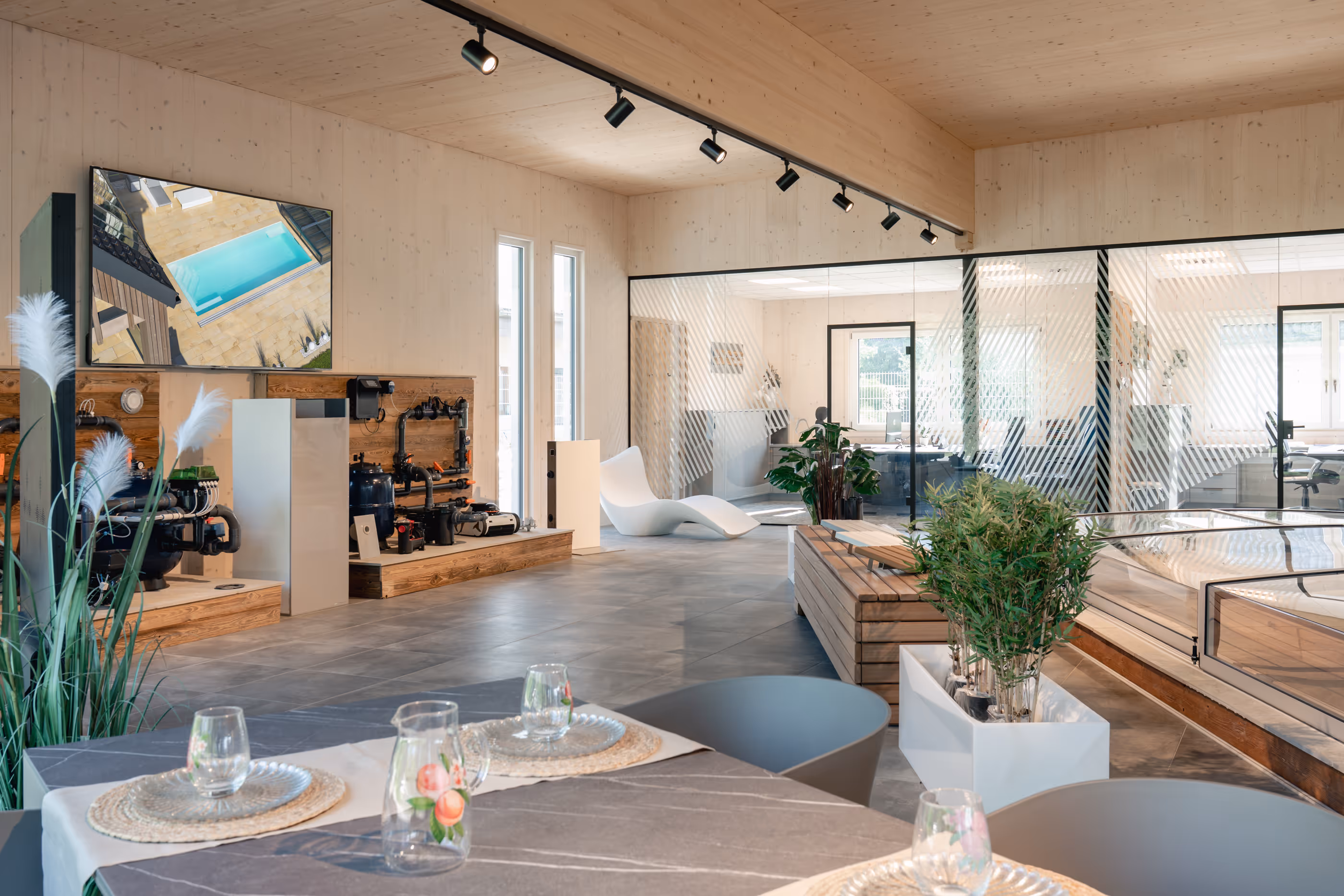 Moderne Ausstellungshalle mit Pooltechnik, Glastrennwänden, Pflanzen und einem gedeckten Tisch im Vordergrund.