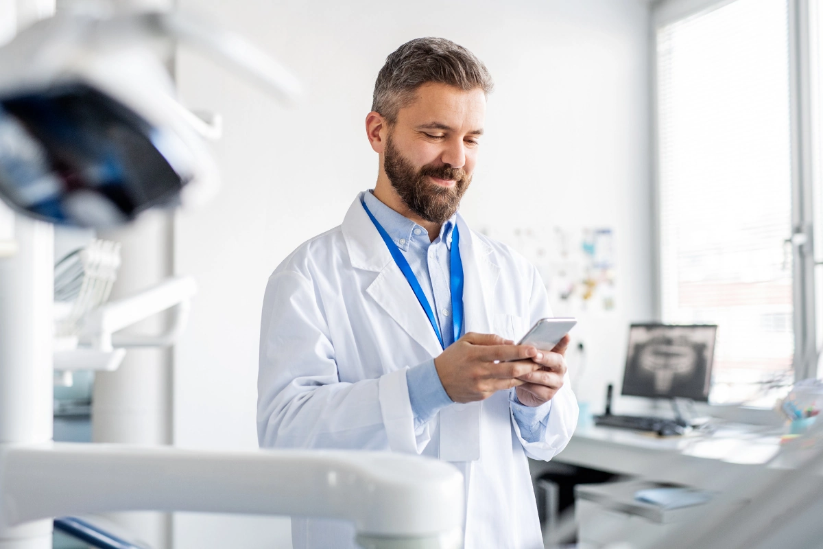 Ein Arzt hält ein Smartphone in der Hand und grinst.