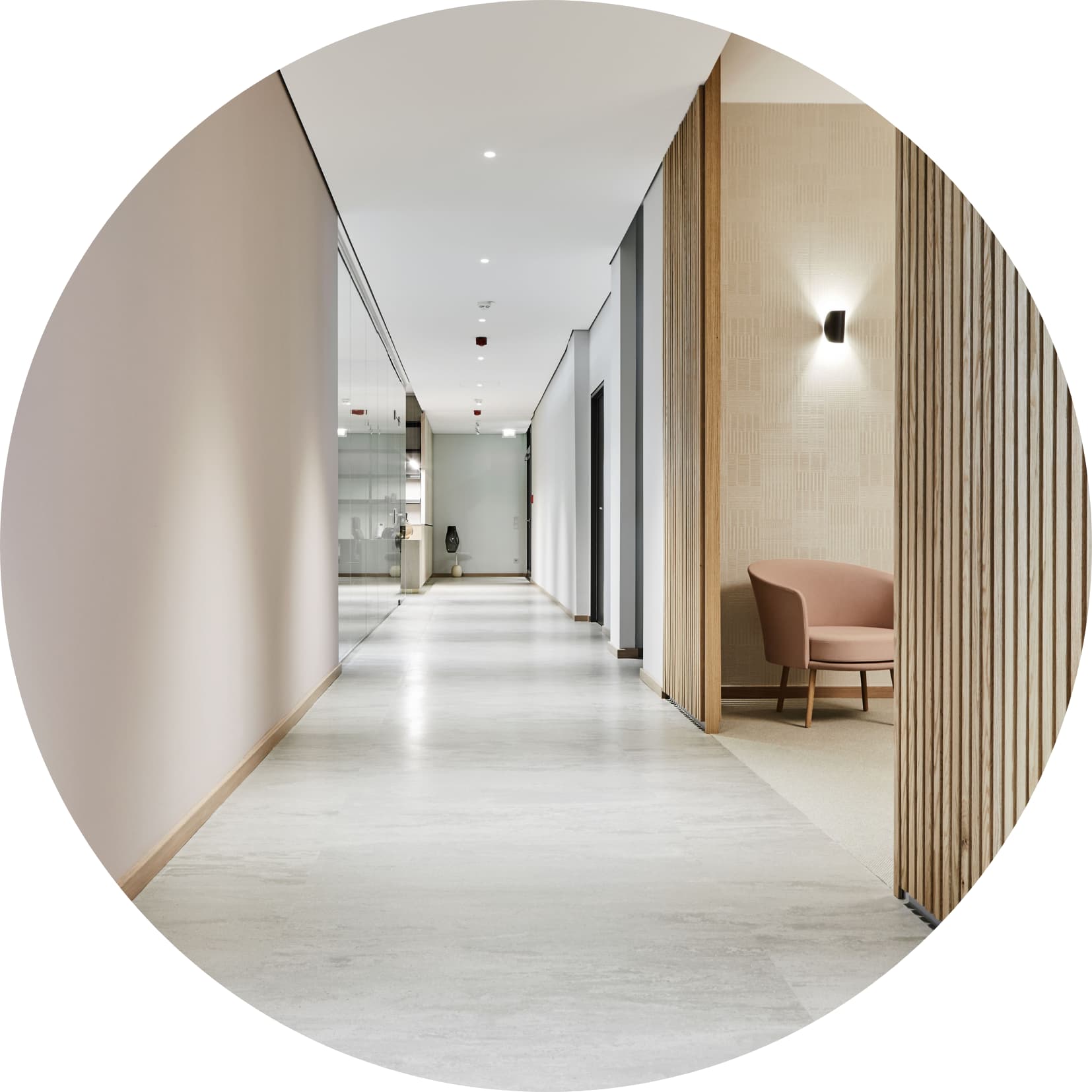 Heller, moderner Praxisflur mit glatten Böden, einer Glaswand auf der linken Seite und einer kleinen Sitzecke mit rosafarbenem Sessel auf der rechten Seite.