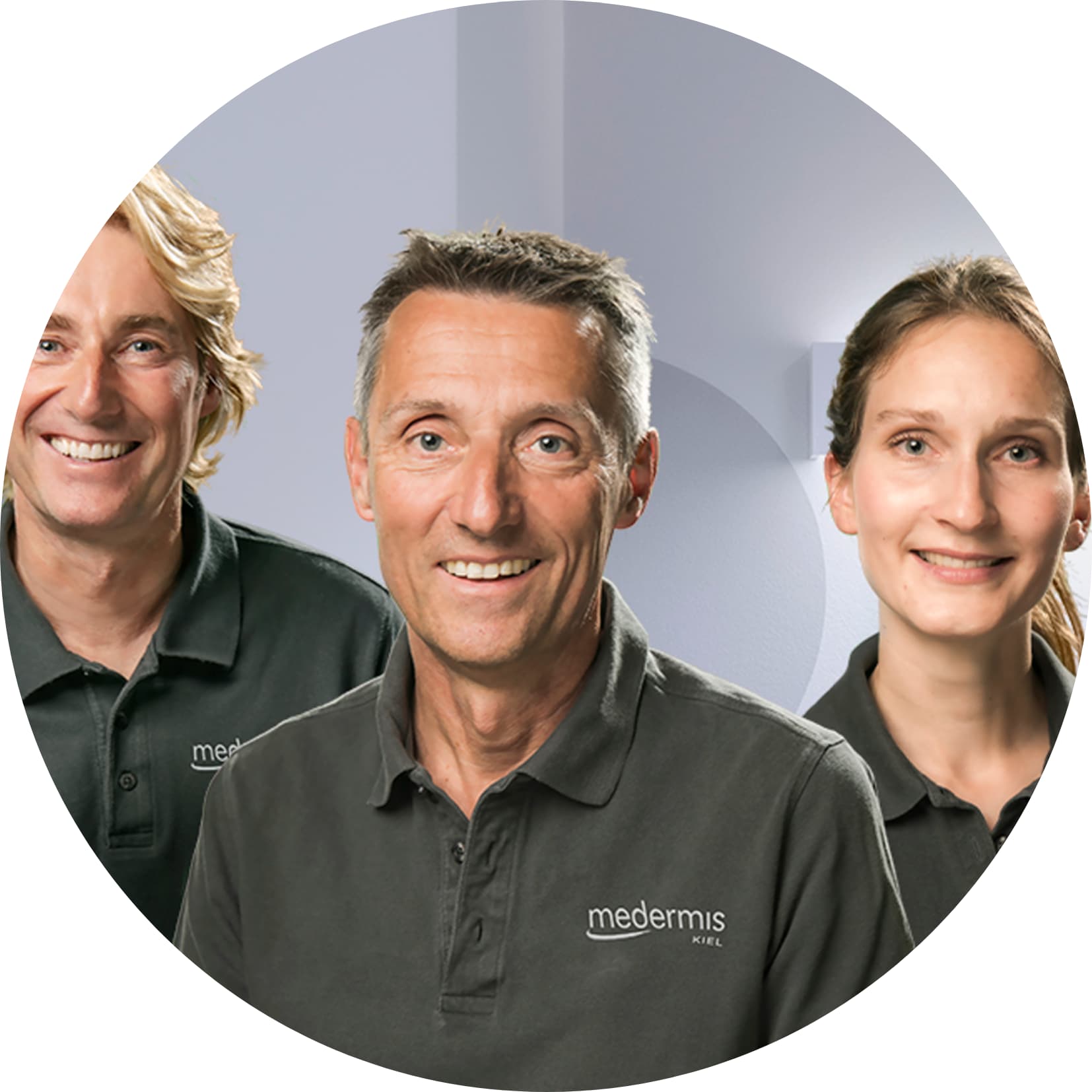 Gruppenporträt von drei lächelnden Personen in dunkelgrauen Poloshirts vor einem hellen, modernen Hintergrund.