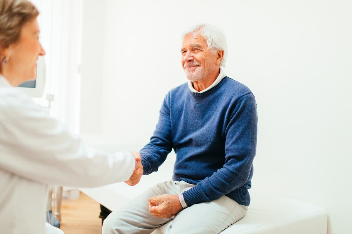 Älterer Mann gibt einem Arzt freundlich die Hand während eines Praxisbesuchs.
