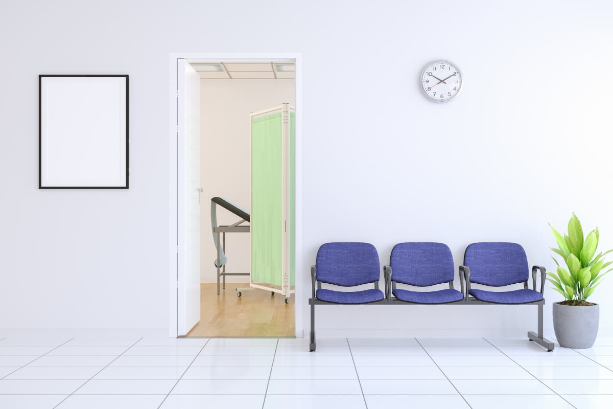 Heller Praxis-Wartebereich mit drei blauen Stühlen, Wanduhr, Pflanze und offener Tür zu einem Behandlungsraum.