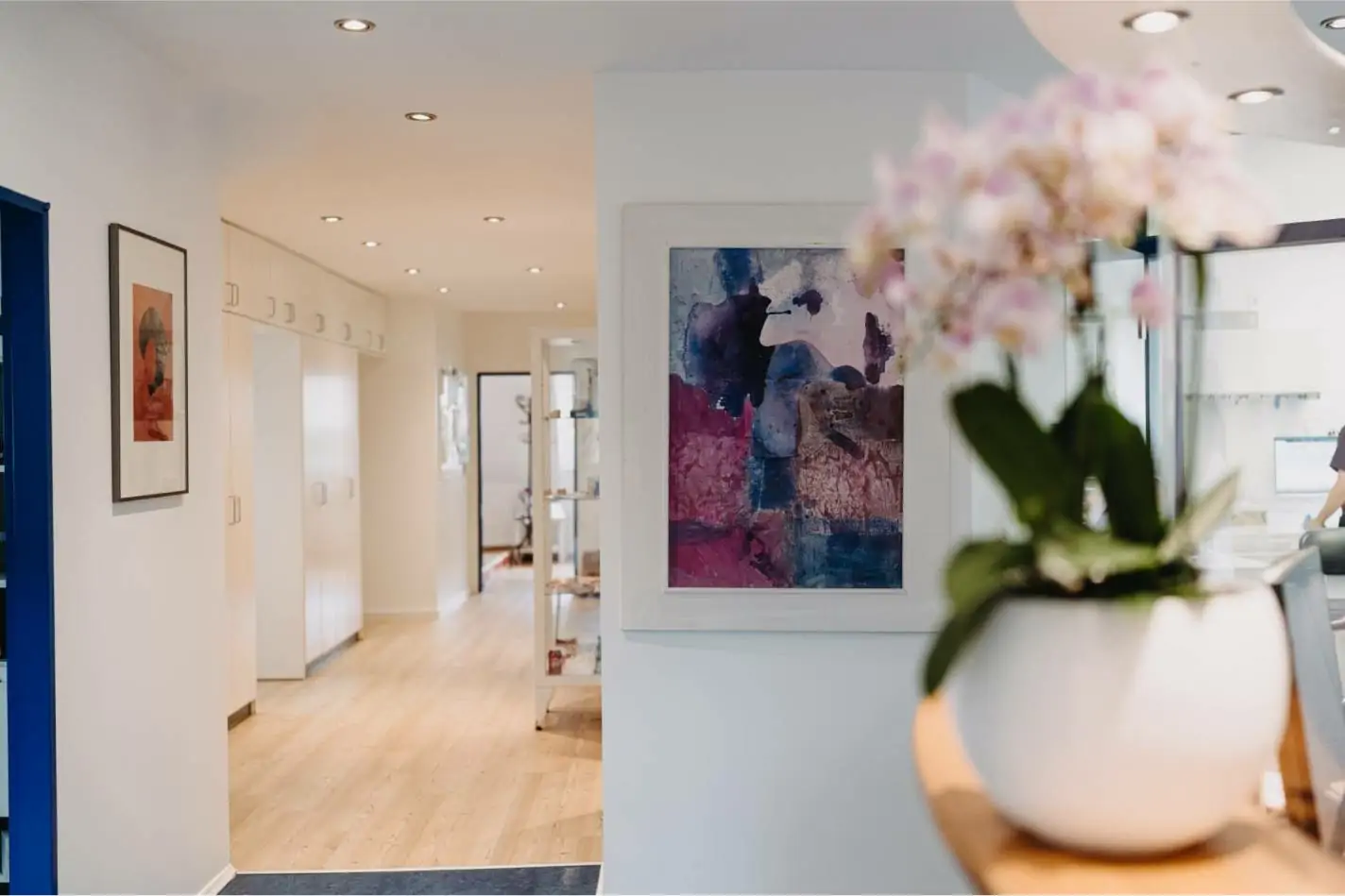 Moderner, heller Eingangsbereich einer Zahnarztpraxis mit Flur, Kunst an den Wänden und einer unscharfen weißen Orchidee im Vordergrund.