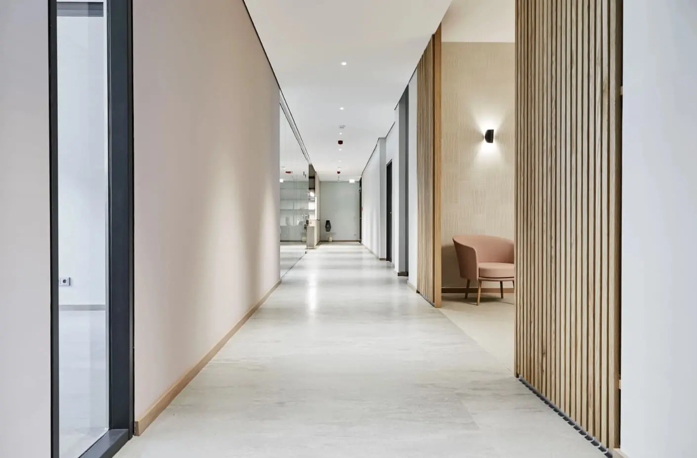 Heller, minimalistischer Flur einer Zahnarztpraxis mit Holzlamellen, modernen Wandleuchten und Blick auf mehrere Behandlungs- oder Praxisräume.