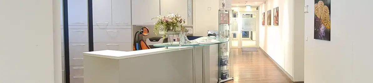 Heller Empfangsbereich einer Zahnarztpraxis mit Rezeption, Flur und moderner Inneneinrichtung.“