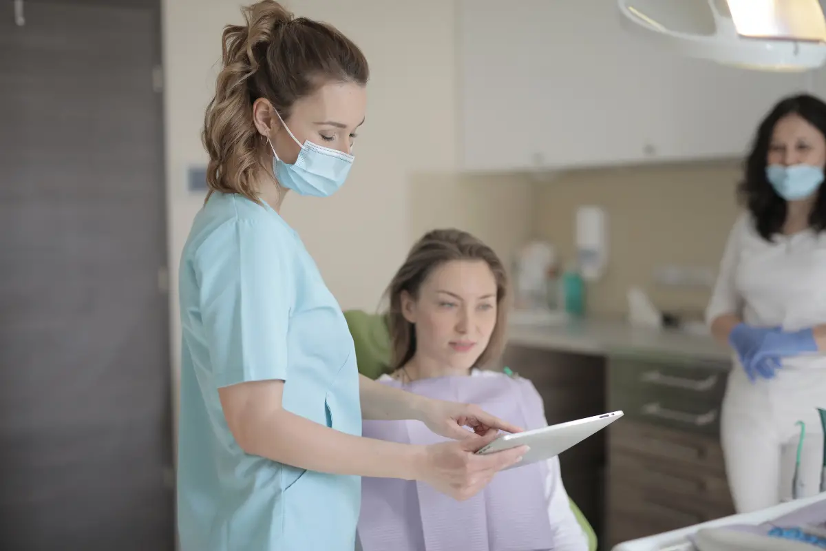 ZFA zeigt einer Patientin in der Zahnarztpraxis Informationen auf einem Tablet — digitale Patientenaufklärung im Praxisalltag.