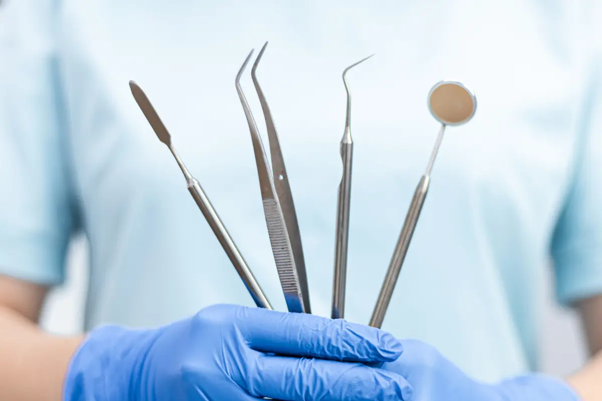 Zahnärztin mit blauem Einmalhandschuh hält zahnärztliche Instrumente wie Sonde, Pinzette und Mundspiegel in der Hand
