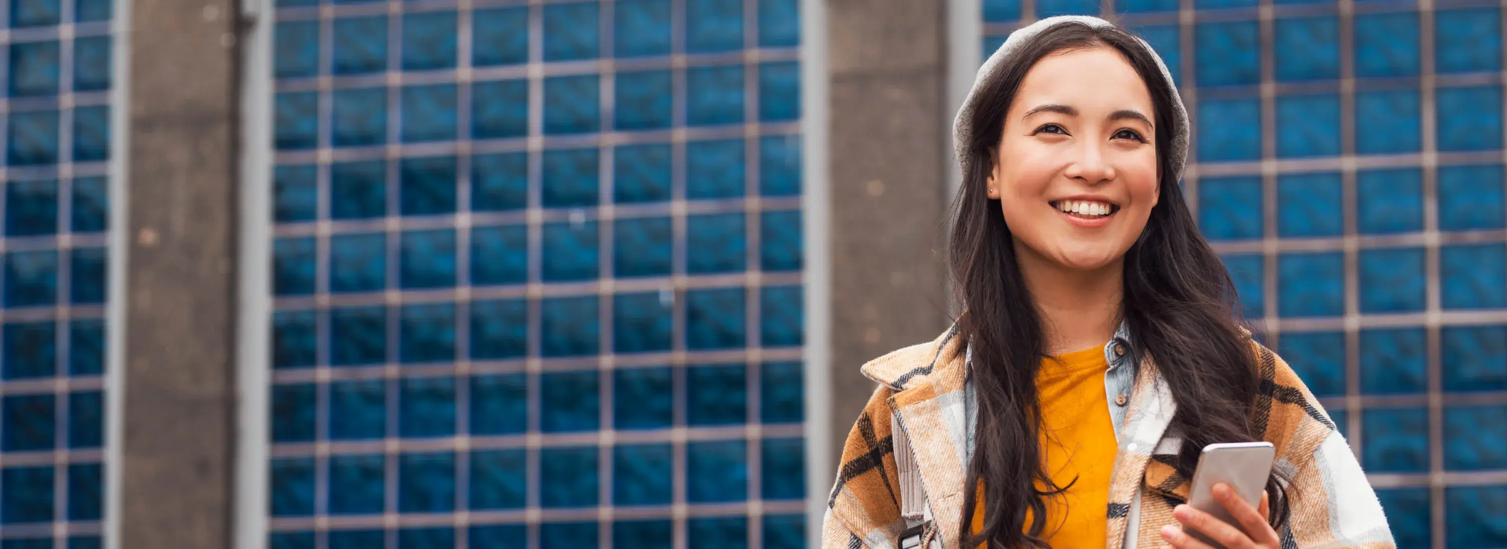 A woman standing in front of a building holding a cell phone.