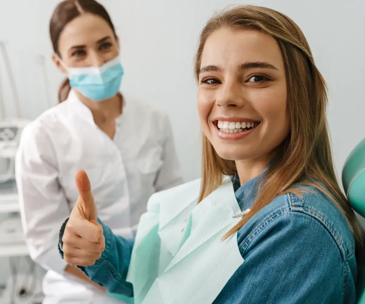 A woman in a dentist's chair giving a thumbs up.
