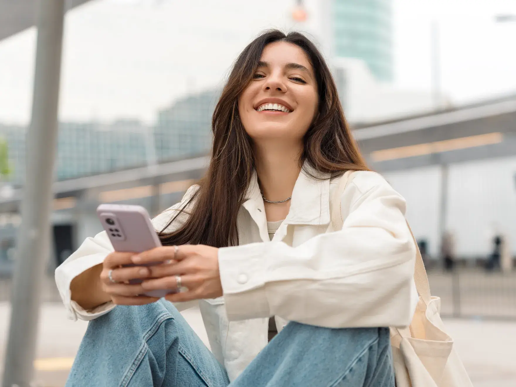 A woman sitting on the ground looking at her cell phone.