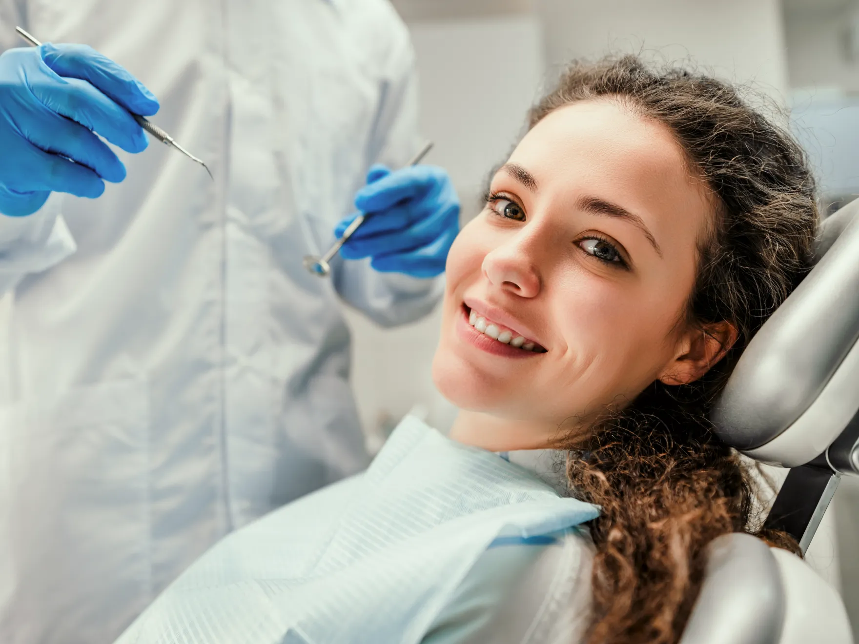 A woman sitting in a dentist chair with a toothbrush in her mouth.