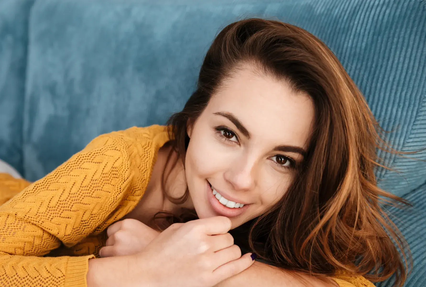 A beautiful young woman laying on top of a blue couch.