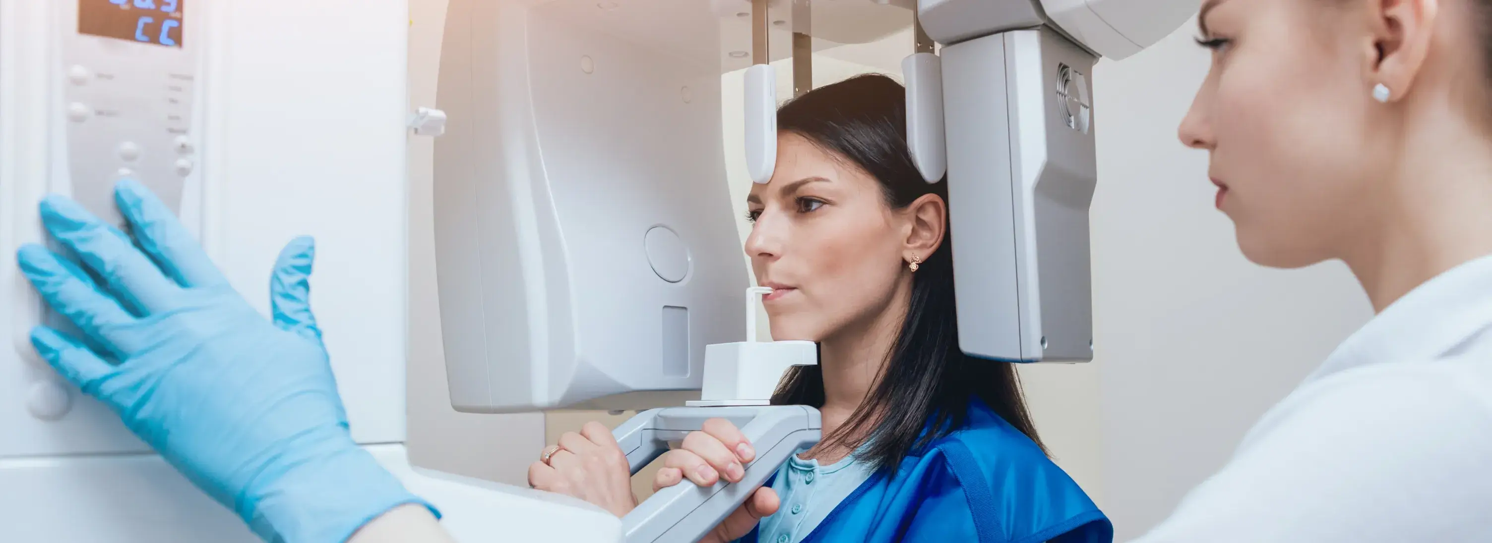 A woman in blue scrubs her face in front of a mirror.