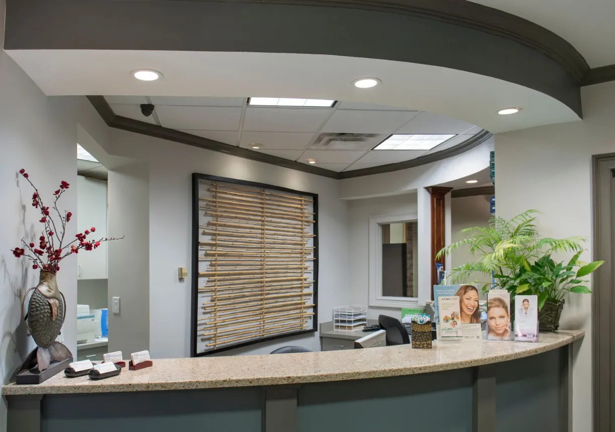 Reception desk with decorative fish sculpture, brochures, and green plants in a modern office interior.