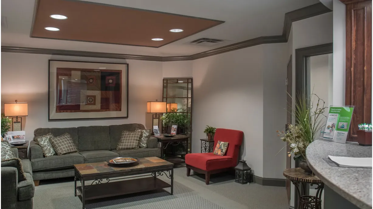 Cozy living room with gray sofas, a red armchair, a coffee table, two lamps, and framed artwork on the wall.