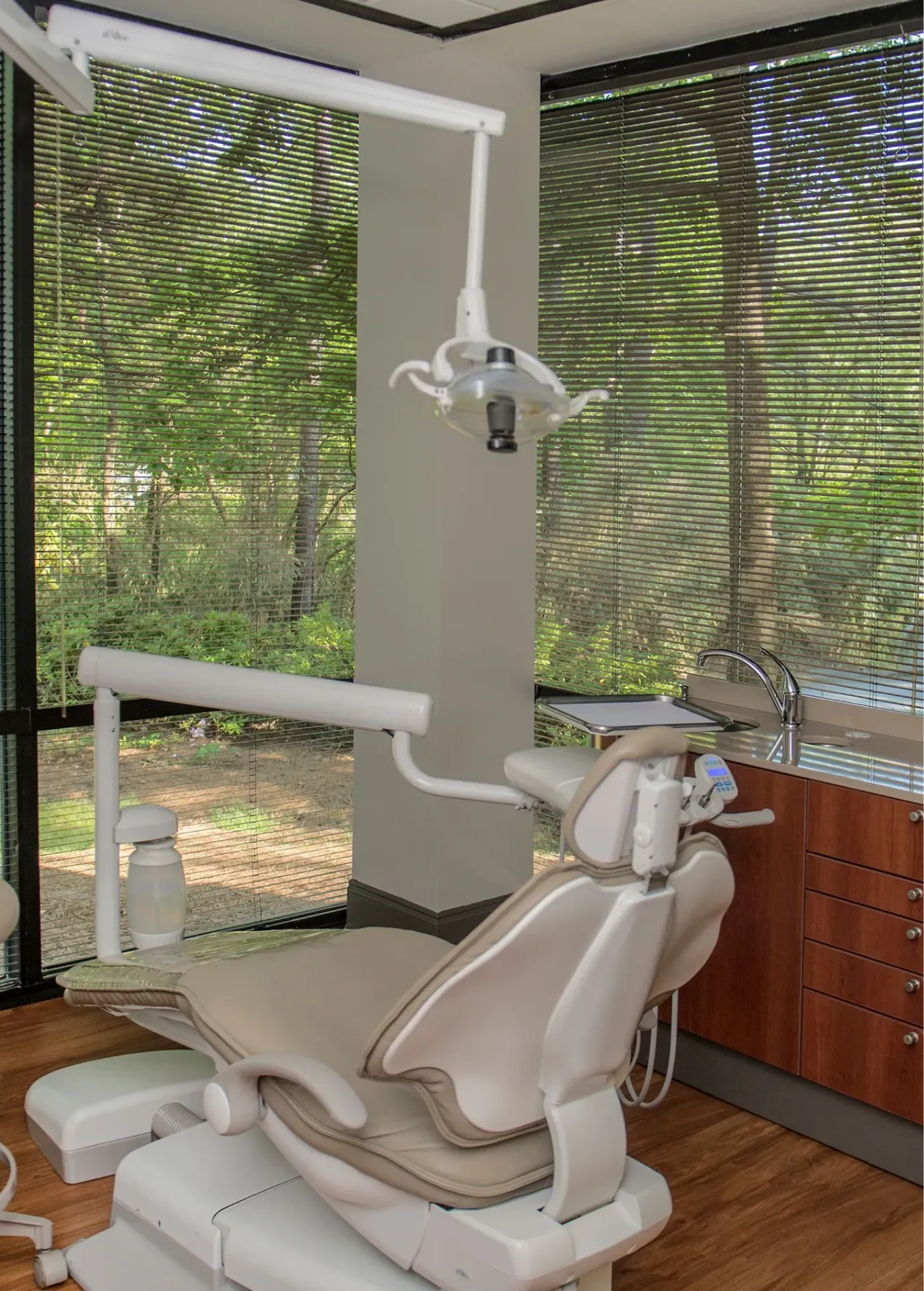 Modern dental chair in a clinic room with large windows showing green trees outside.