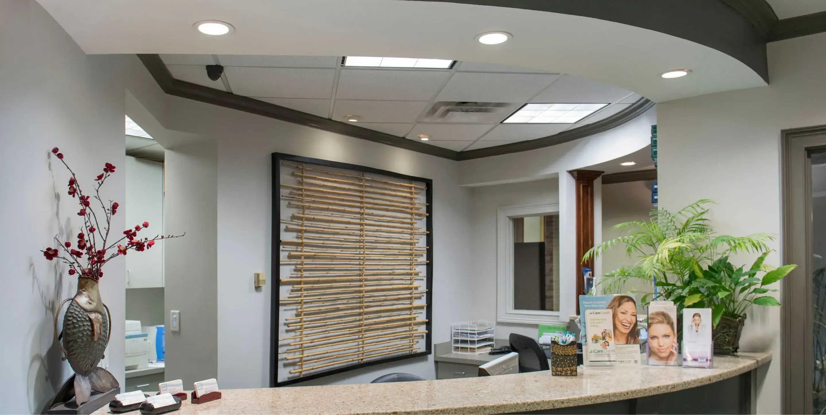 Reception desk with a metal fish sculpture vase with red flowers, informational brochures, and a green plant in a modern office setting.