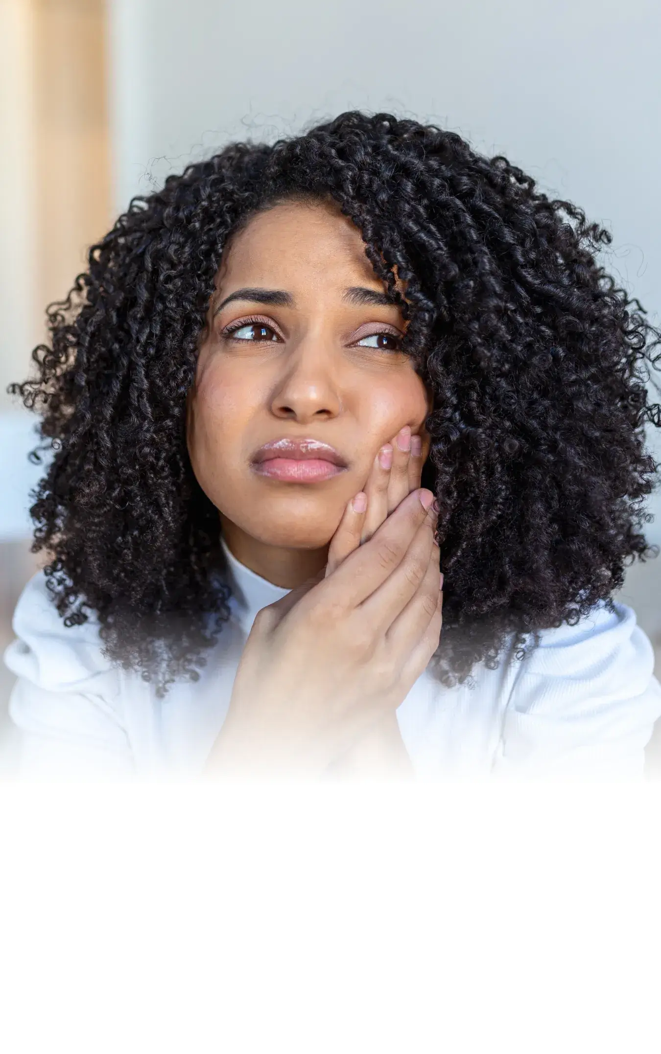 Woman with curly hair holding her cheek in pain, indicating a toothache.